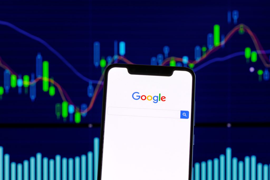 Google logo is seen on a smartphone over a stock chart